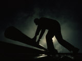 Silhouetted Oil Rig Worker Lifting a Pipe, Wyoming Photographic Print by Lynn Johnson