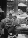 Father Sitting on Couch with Pigtailled Daughter Reading to Her the Sunday Comic Pages Lámina fotográfica por Nina Leen