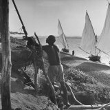 Man Working with Irrigation System as Sailboats Sit at Edge of Nile River at Wadi Halfa Fotografisk tryk