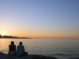 Couple Sitting on Sea Wall Watching Sunset Photographic Print by Miller John