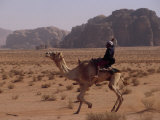 Young Bedouin Races His Camel Below Huge Towers in Arabian Desert Photographie par Gordon Wiltsie