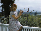 As Girl Fills One Bird Feeder Vial, a Hummingbird Sips from Another Photographic Print by Edwin L. Wisherd