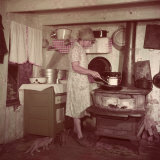 Woman Stands at Old-Fashioned Stove to Cook, Cats Prowl at Her Feet Photographic Print by Justin Locke