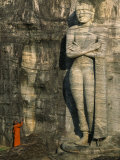Buddhist Monk at the Foot of a Tall Stone Buddha Sculpture on a Hill Photographie par Paul Chesley