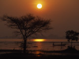 Silhouetted Men in a Canoe at Sunset on Calm Water Photographie par Paul Chesley