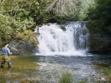 Man in Boots Casts a Line by a Waterfall as He Fishes for Trout Photographie par Jack Fletcher