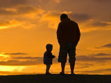 Father and His Baby Son Watch the Sunrise from a Coastal Hilltop Photographie par Jason Edwards