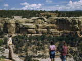 Tourists Stand on a Canyon Rim Overlooking Ancient Cliff Dwellings Photographie par Willard Culver