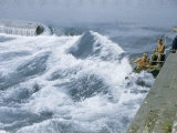 Men Paddle Narrow Channel Between Rocks and Wall Along Riverbank Photographie par Walter Meayers Edwards