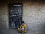 Afghan Refugee Youth Sits on the Ground Holding a Baby in Front of a Shop in Pakistan Photographie