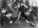 Two Boys Sit for a Game of Chess. Eight Spectators Look On Photographic Print