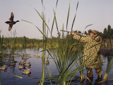 Hunter Aiming Rifle at Flying Duck Photographic Print by Dennis Hallinan