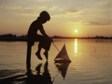 Silhouette of Boy Sitting at Pier with Toy Sailboat Photographic Print by Dennis Hallinan