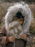 A Nunamiut Boy in a Fur-Trimmed Parka Holds a Mask of Caribou Hide Photographie par Thomas J. Abercrombie