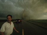 A Tornado Barrels Down a Road Towards a Tornado Chaser Photographie par Carsten Peter