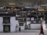 A Monk Walks Past a Small Village Sloping Upwards on the Hills Photographie par Jimmy Chin