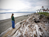 Woman Standing on Driftwood and Looking Towards Discovery Park Lighthouse Photographie par Micah Wright