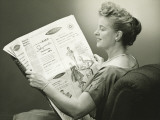 Woman Sitting in Armchair, Reading Newspaper, Smiling Photographic Print by George Marks