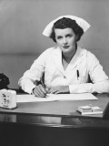 Young Nurse Sitting at Desk, Writing Photographie par George Marks