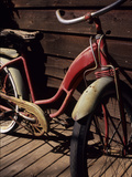 A Very Old Red Girls' Bike Rests on an Old Wooden Porch Photographie par Paul Damien