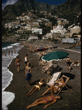 Sunbathers Lounge on a Pebbled Beach by Whitewashed Houses on a Cliff Impressão fotográfica por Luis Marden