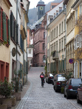 A Woman Rides a Bike Up a Cobbled Street in the Morning Photographic Print by Greg Dale