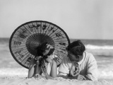 1920s Romantic Couple Looking At One Another Laying Face To Face Under Parasol On Sandy Beach Photographie par H. Armstrong Roberts
