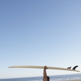 Head and arms of man carrying surf board above head at beach Fotografie-Druck von John Lund