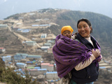 A Woman Carries Her Baby in a Blanket with Namche Visible Behind Photographic Print by Alex Treadway