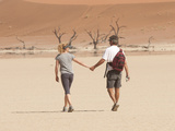 A Couple Holds Hand While Walking Through a Sand Dune Park in Namibia Photographie par Pete McBride